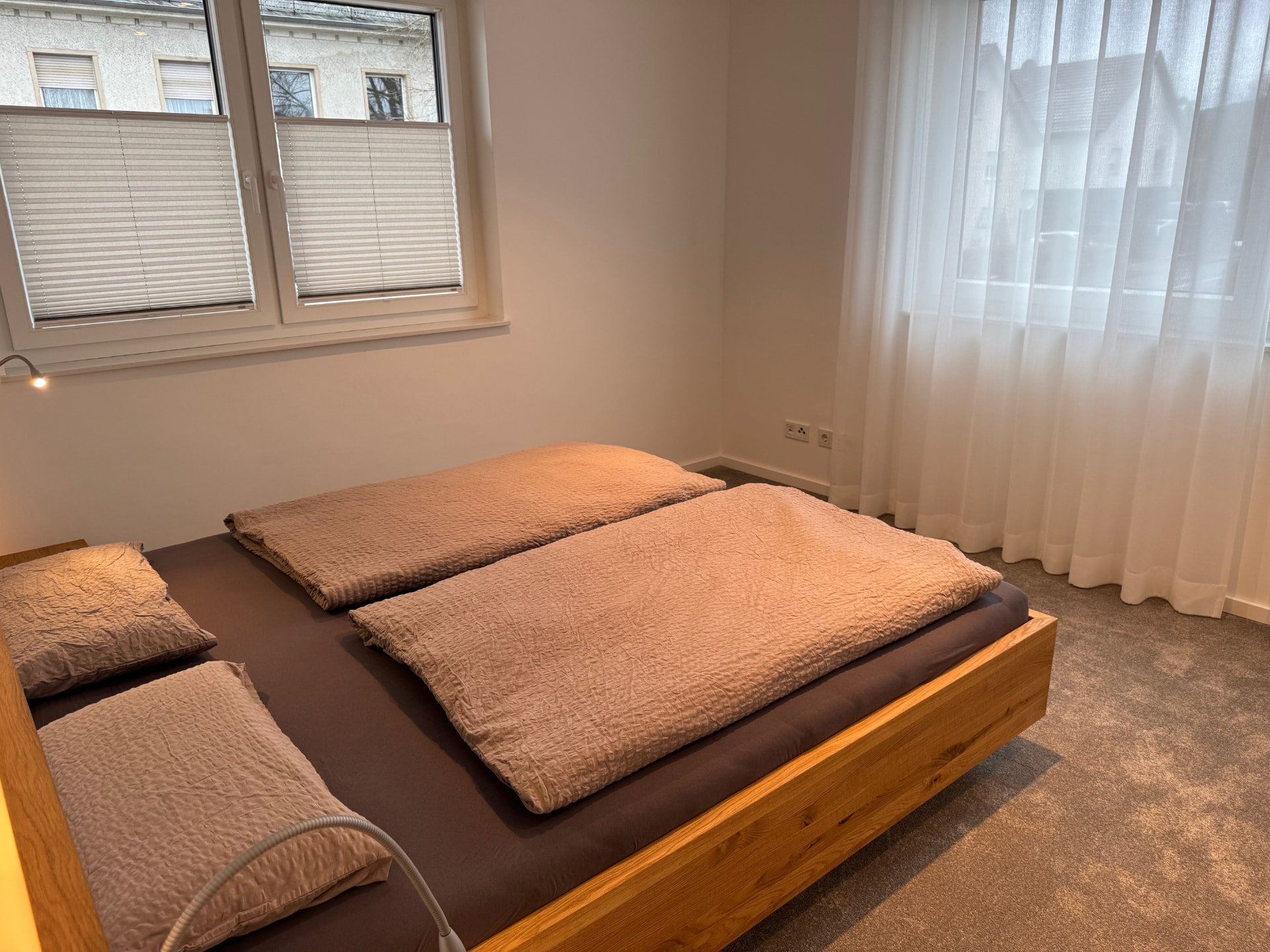 Schlafzimmer mit Doppelbett aus Eiche, Leselampen und bodentiefem Fenster.