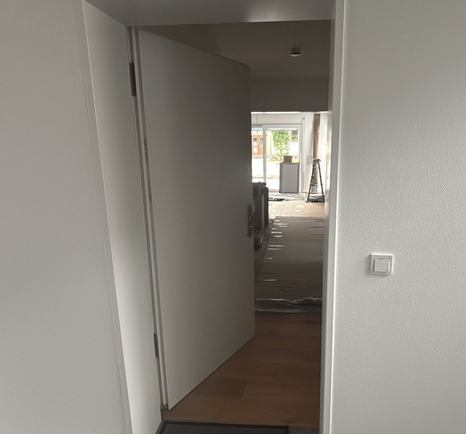Eine weiße Tür steht offen und zeigt einen Flur mit Holzboden und Bauarbeiten im Hintergrund.