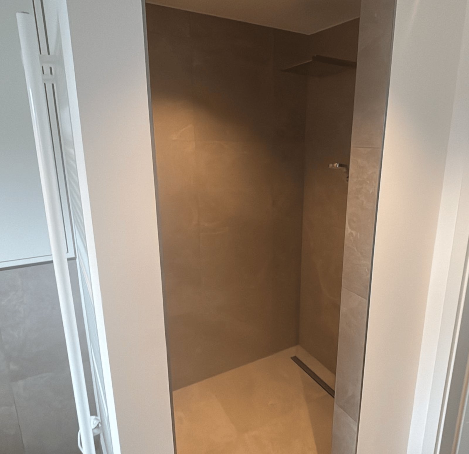 Eine begehbare Dusche mit grauen Fliesen, Duschkopf und einem schmalen Abfluss.