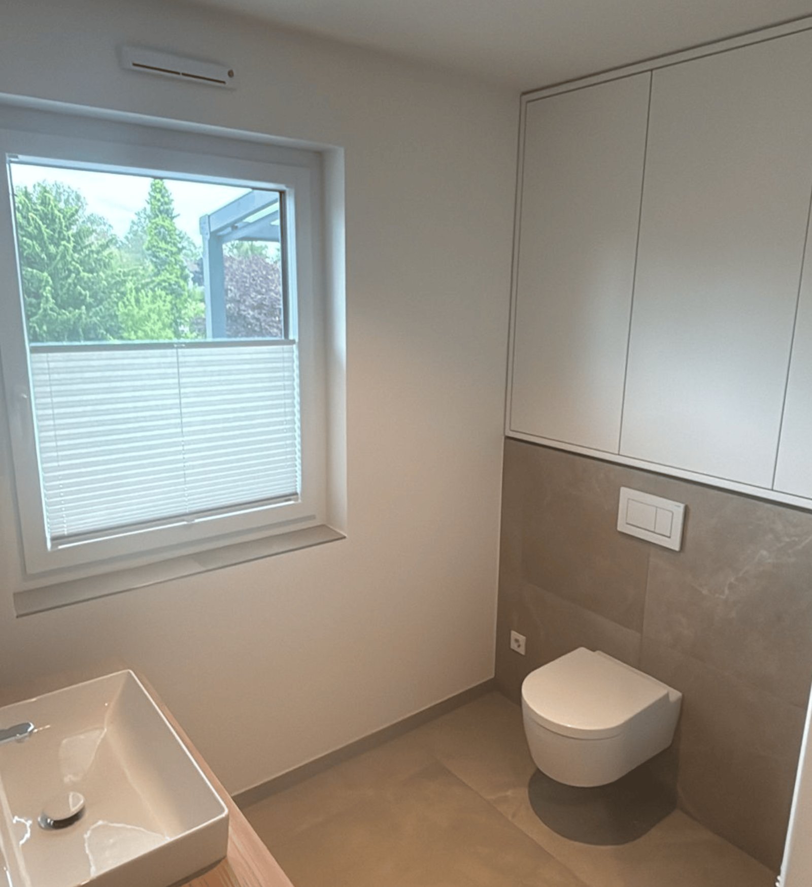 Modernes Bad mit Fenster, Waschbecken, Toilette und weißen Wandschränken.
