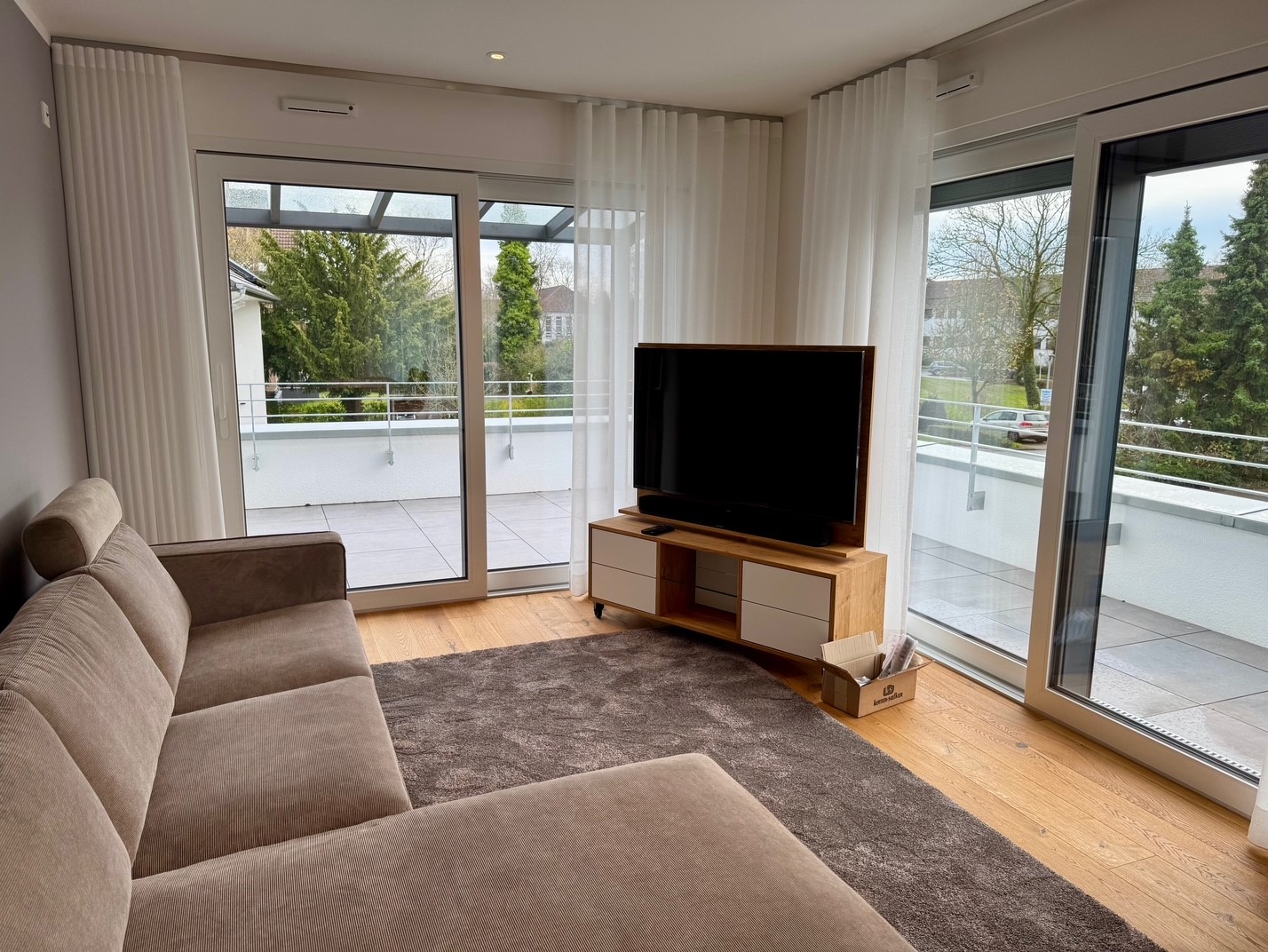 Wohnbereich mit Blick durch die Glastüren auf die überdachte Dachterrasse.