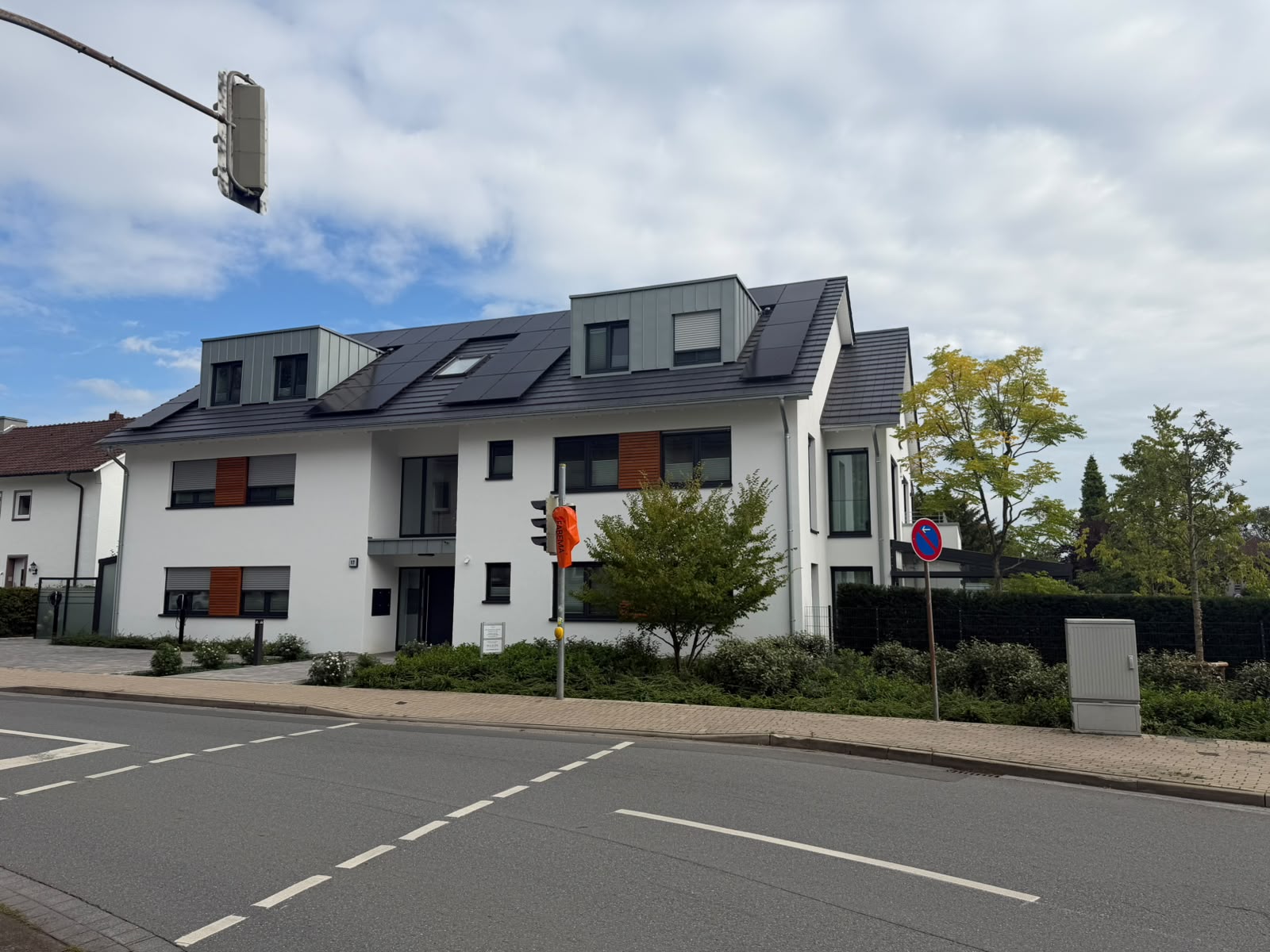 Ansicht der weißen Fassade mit dunklem Satteldach, Gauben und integrierten Solarpaneelen von der Straße aus.