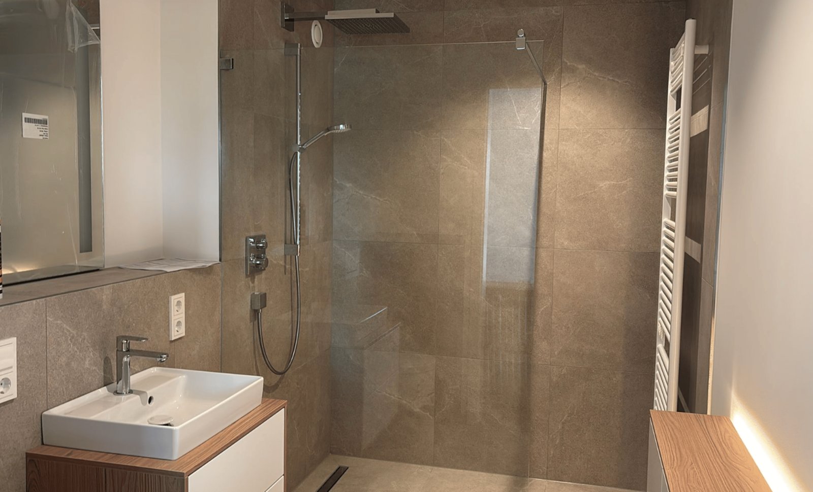 Modernes Badezimmer mit begehbarer Glasdusche, weißem Waschbecken auf Holzunterschrank und Handtuchheizkörper.