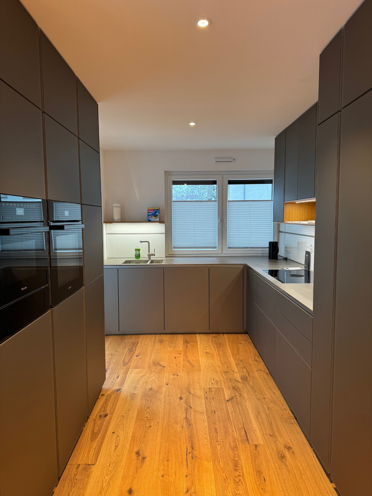 U-förmige Luxusküche mit grauen Fronten, Miele-Backöfen und Eichenboden.