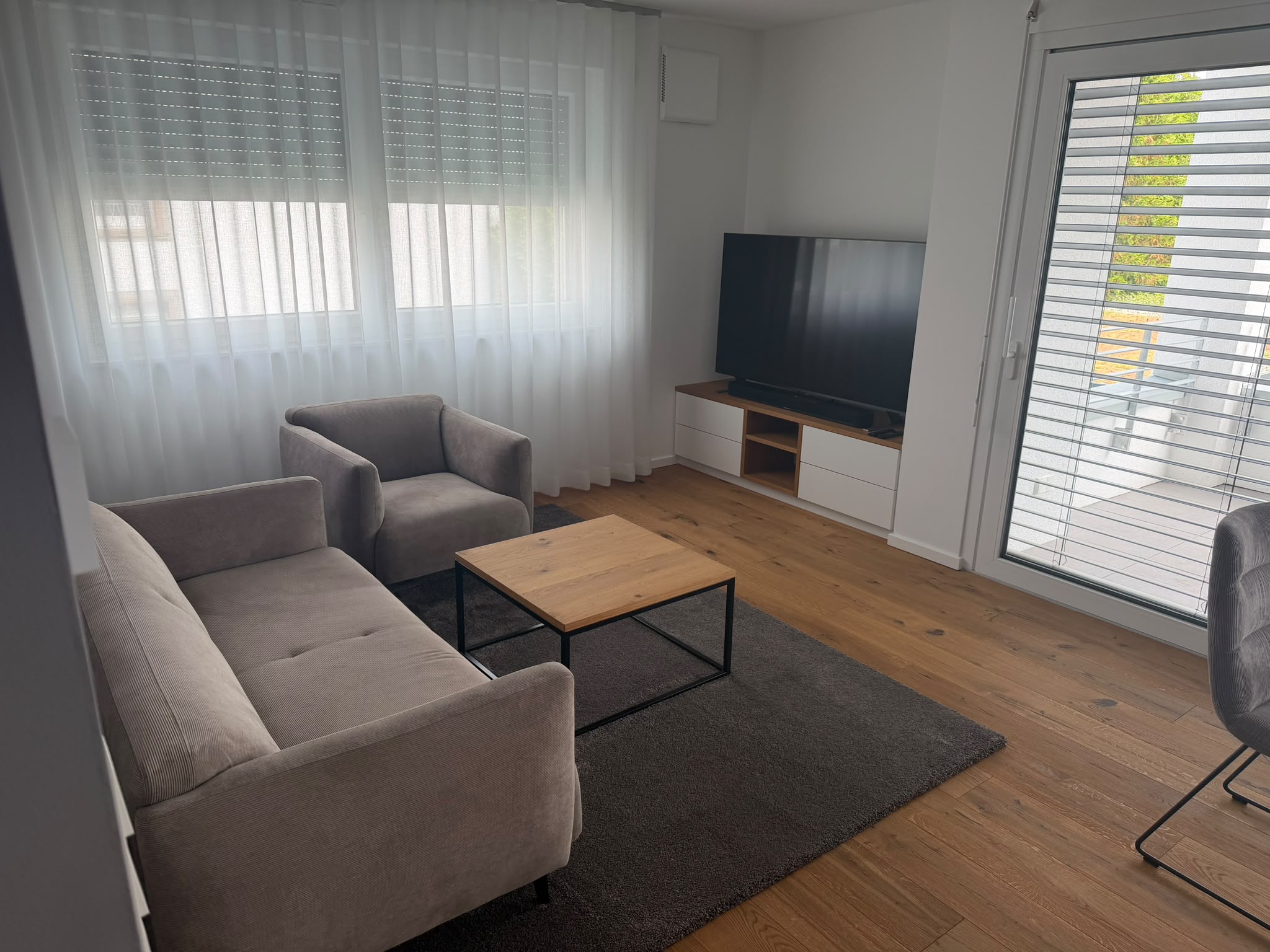 Wohnbereich mit TV-Sideboard, großem Fernseher und Glasschiebetür zum Balkon.