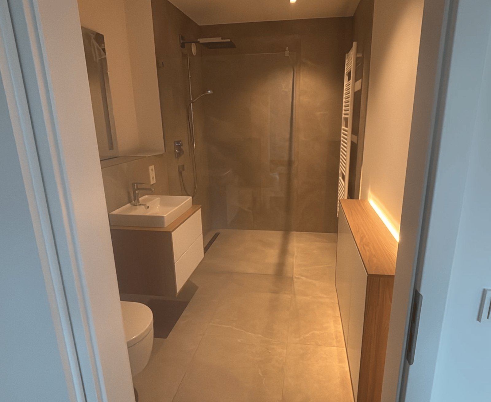 Modernes Badezimmer mit begehbarer Dusche, Waschbeckenunterschrank aus Holz und weißer Front, und beleuchtetem Schrank.