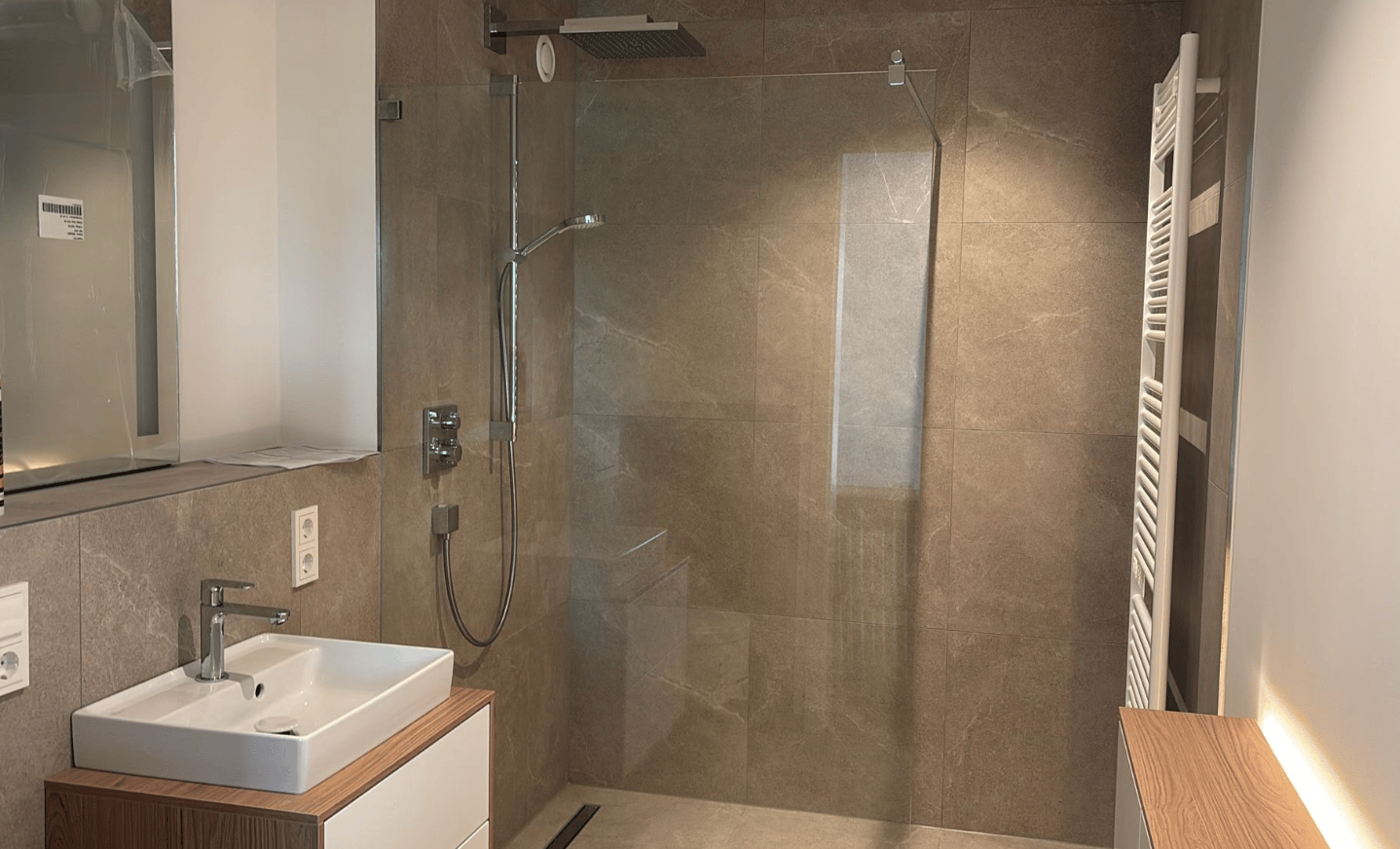 Modernes Badezimmer mit begehbarer Dusche, Waschbecken, Spiegel und Handtuchhalter.