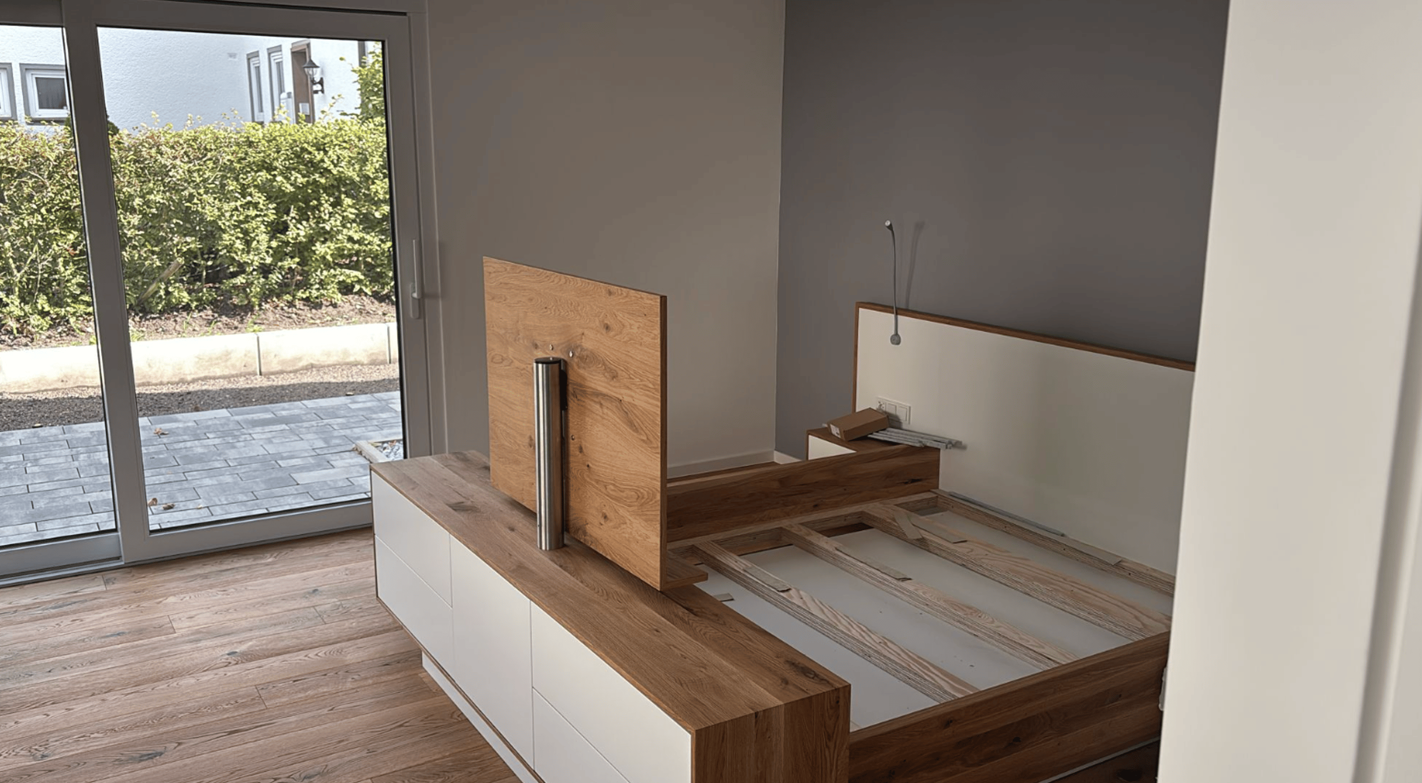 Bett aus Holz und weißem Lack in einem Raum mit Glastür.