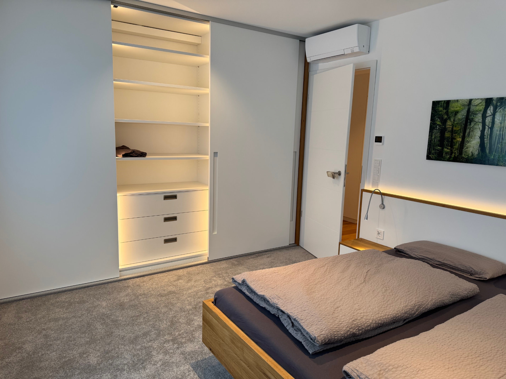 Beleuchteter weißer Einbauschrank mit Regalen und Schubladen im Schlafzimmer.