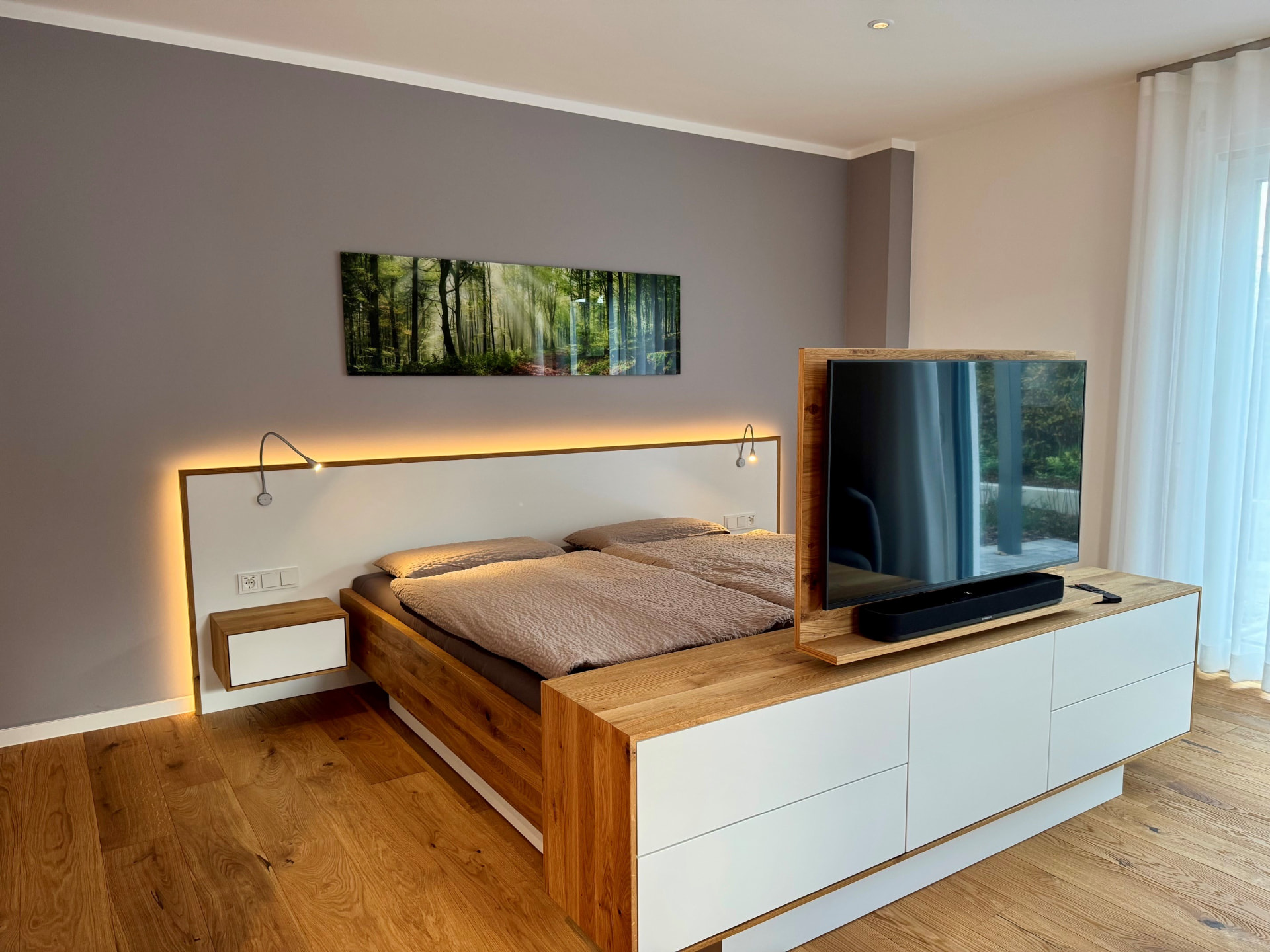Doppelbett aus Eiche mit beleuchtetem Kopfteil, Nachtkonsole und drehbarem TV am Fußende.