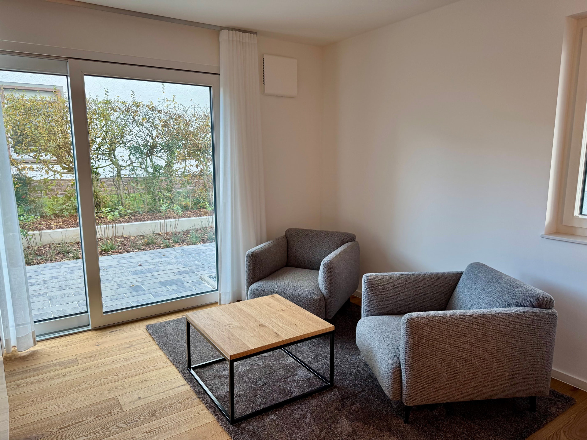 Sitzecke mit zwei grauen Sesseln, Couchtisch aus Eiche und bodentiefer Fenstertür zur Terrasse.