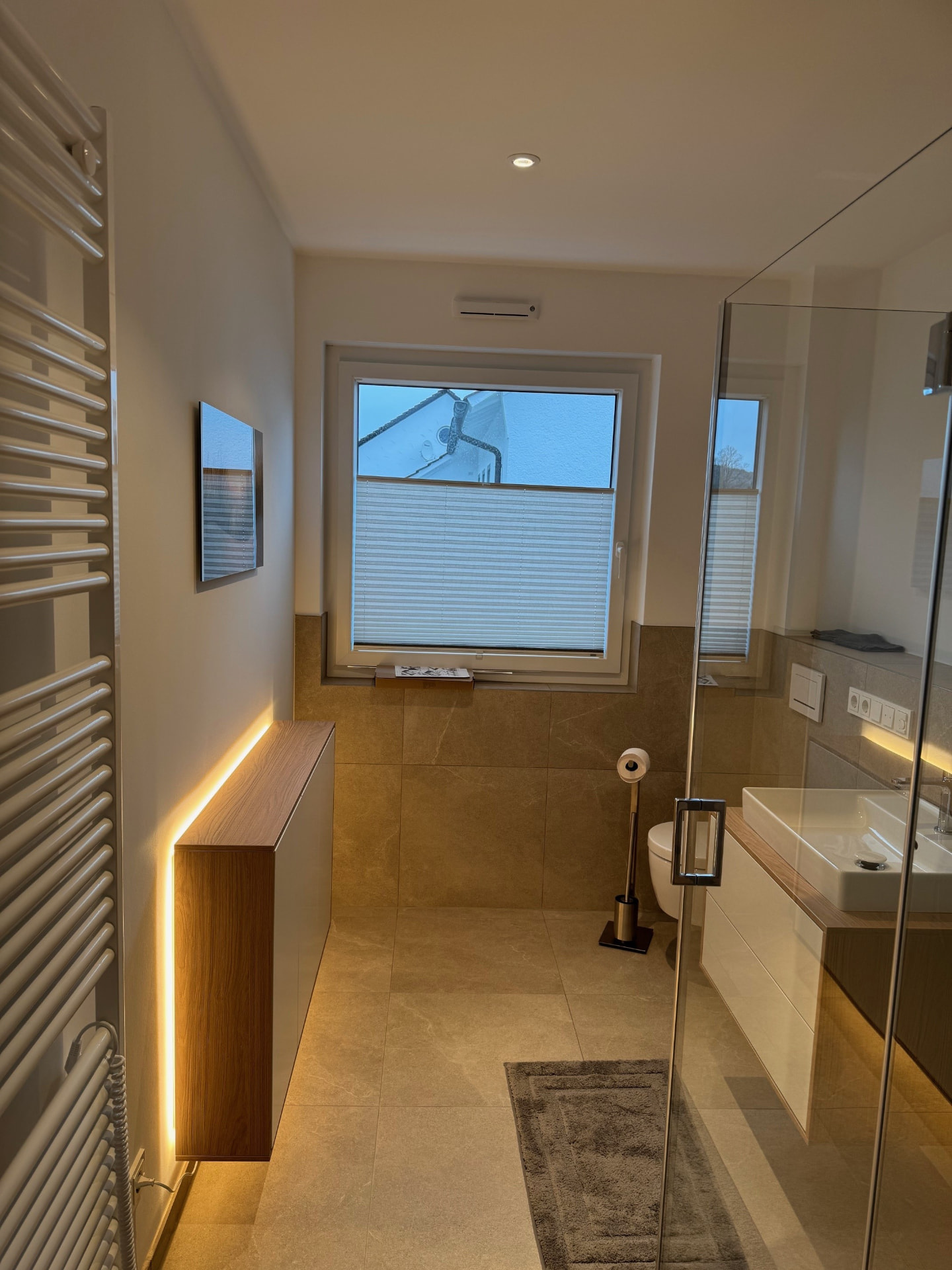 Bad mit Handtuchheizkörper, beleuchtetem Sideboard, Wand-WC und Fenster.
