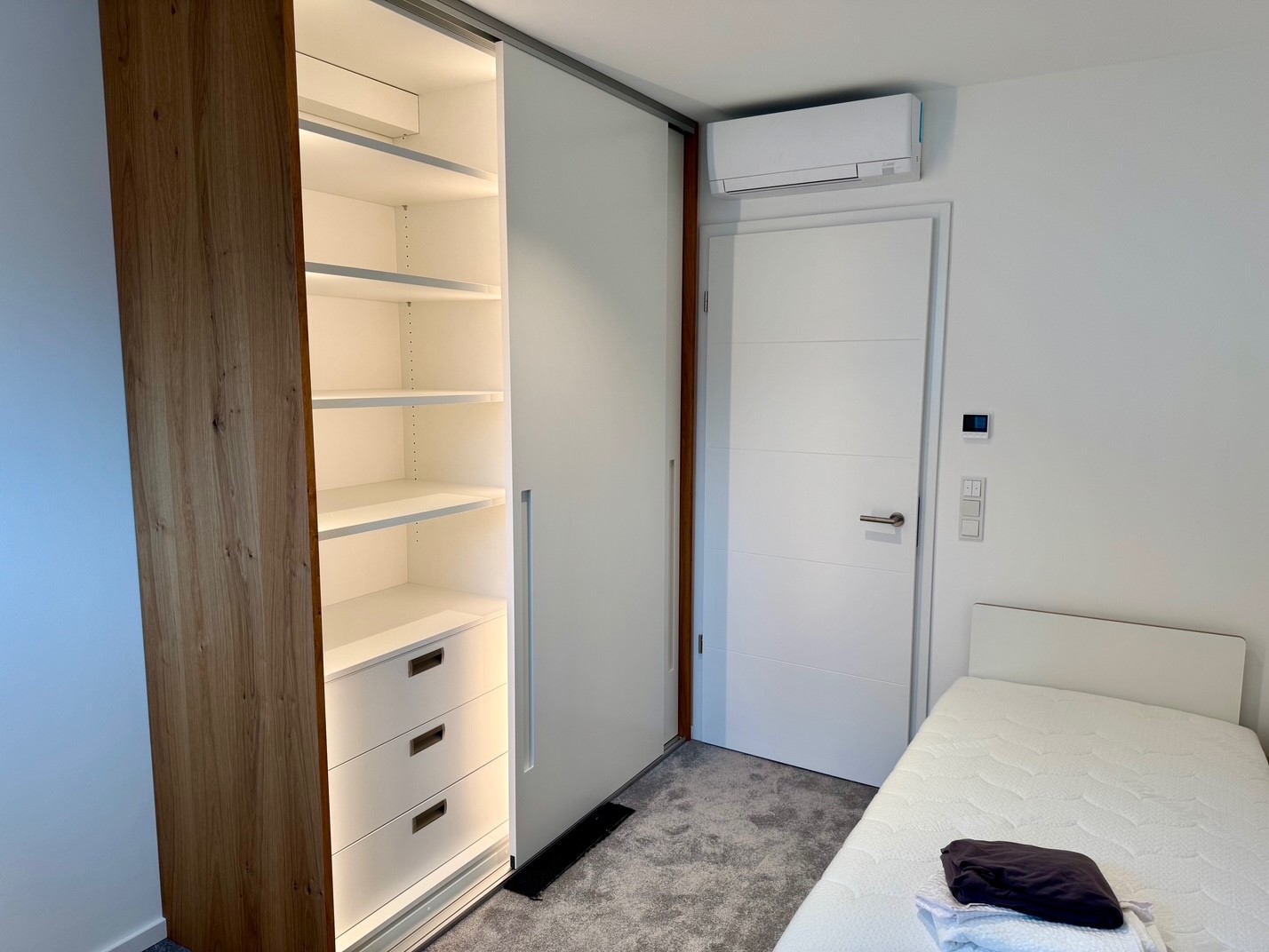 Gästezimmer mit Einzelbett und beleuchtetem Einbauschrank mit Schiebetüren.