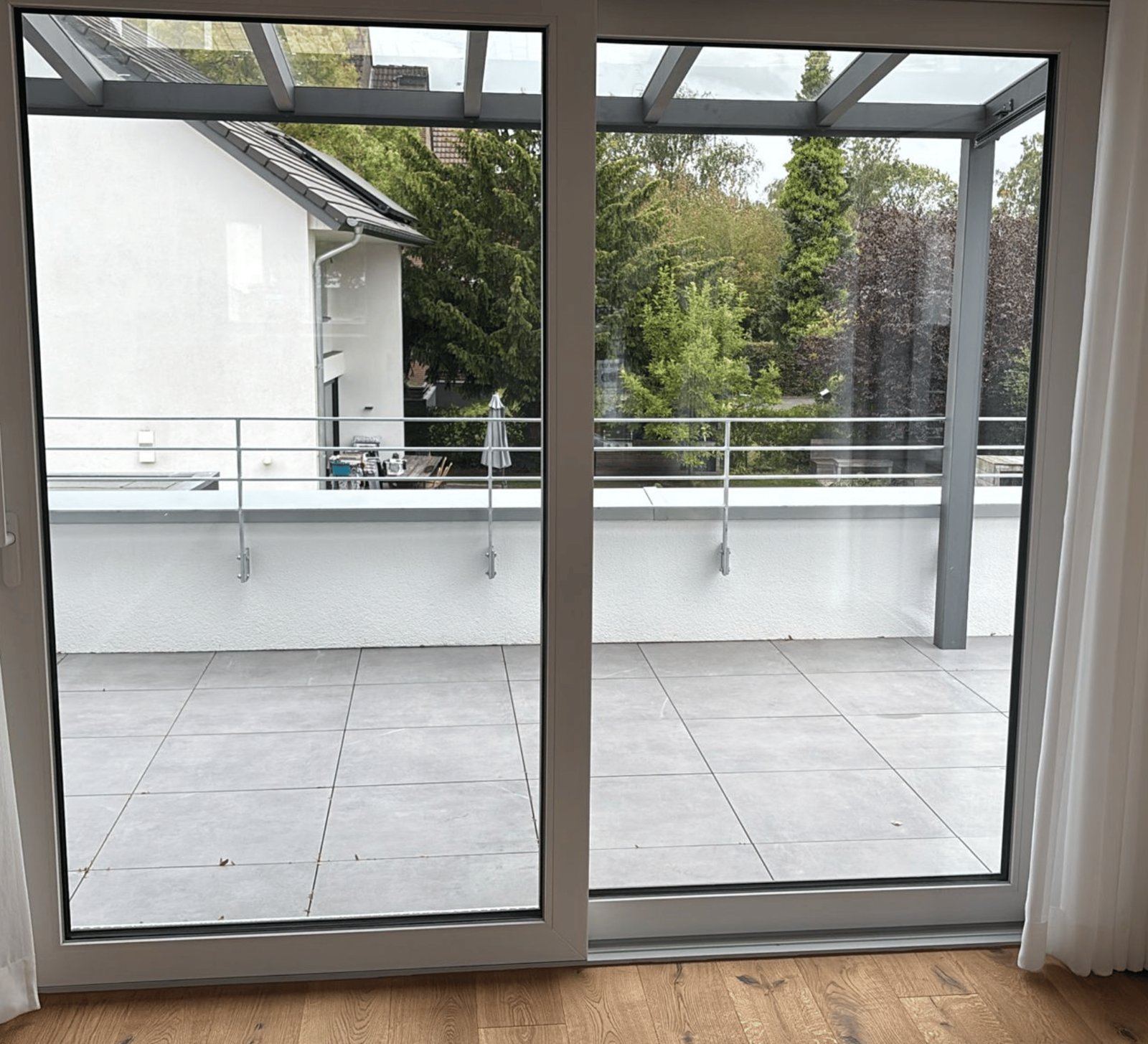 Glasschiebetüren öffnen sich zu einer modernen Terrasse mit Fliesenboden und Geländer.