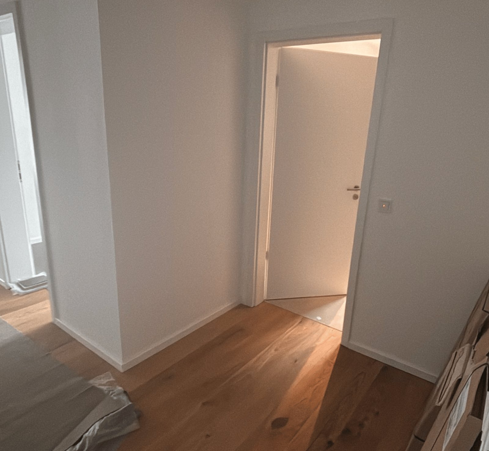 Heller Raum mit Holzboden und offener weißer Tür, Sonnenlicht fällt auf den Boden.