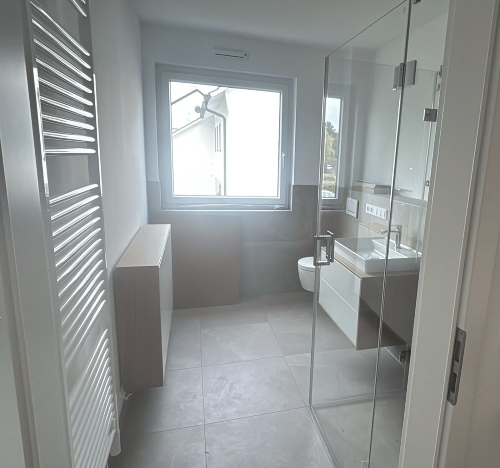 Modernes Badezimmer mit ebenerdiger Dusche, Waschtisch, Toilette und Fenster.