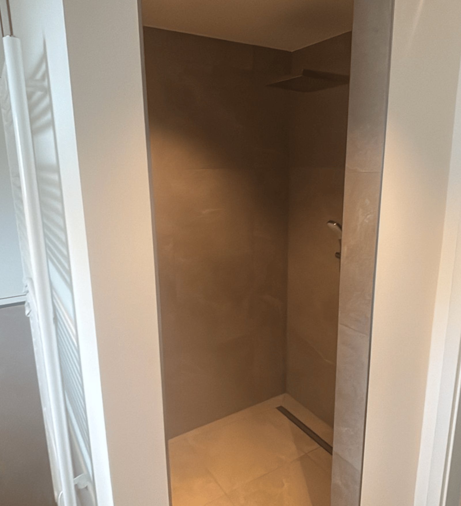 Eingang zu einer begehbaren Dusche mit grauen Fliesen, Duschkopf und Abfluss.