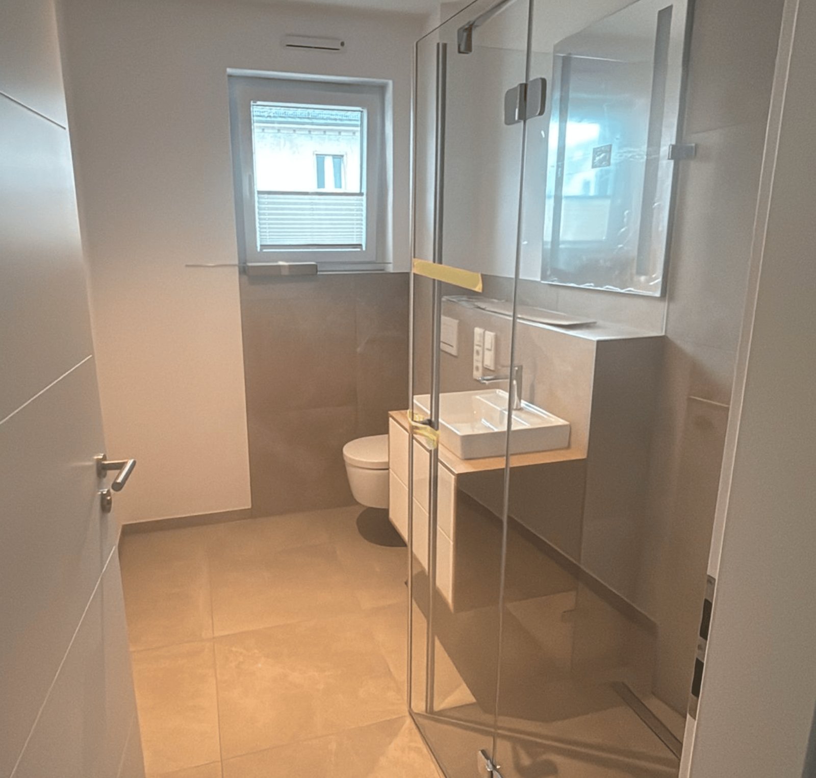 Modernes Badezimmer mit weißer Toilette, Waschbecken auf Holzplatte und Glasdusche.