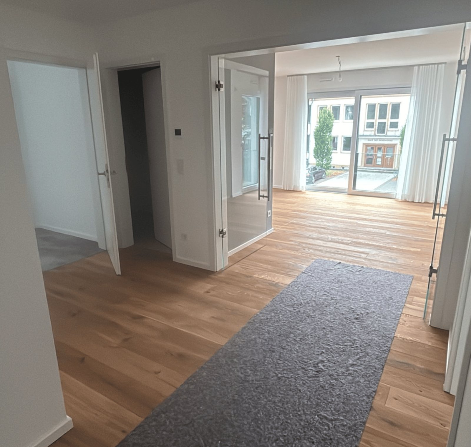 Leerer Flur mit Holzboden und grauem Läufer, der zu einem offenen Wohnbereich führt.