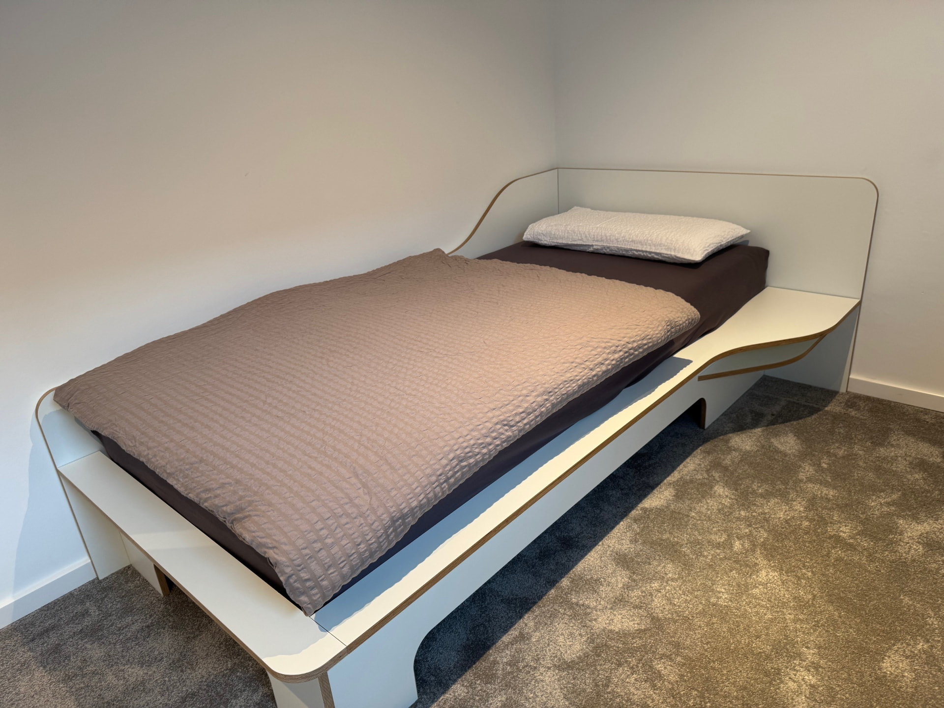 Gästezimmer mit weißem Einzelbett und Teppichboden.