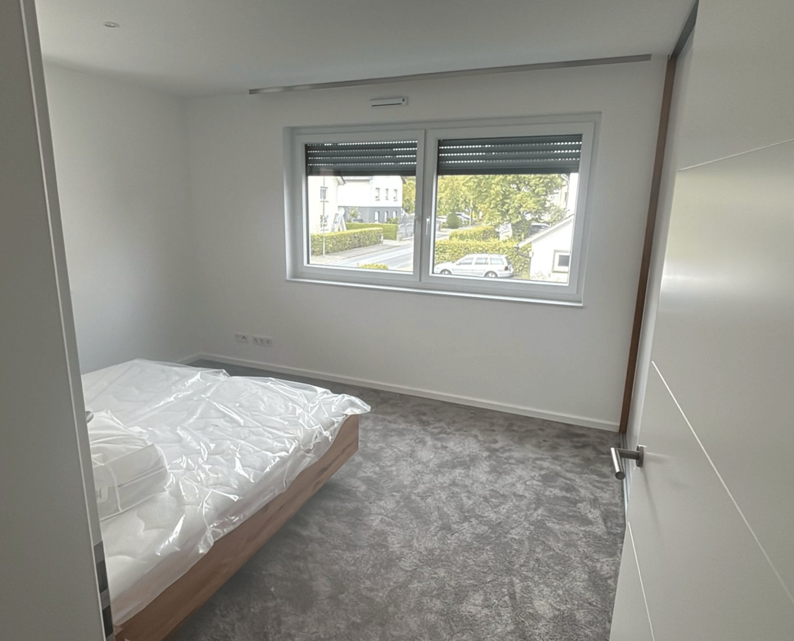 Leeres Schlafzimmer mit grauem Teppich, weiß gestrichenen Wänden und einem Fenster.