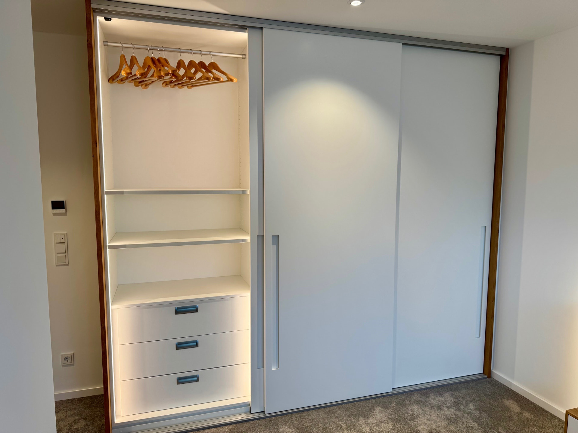 Großer Einbauschrank mit Schiebetüren und beleuchtetem Innenraum im Schlafzimmer.
