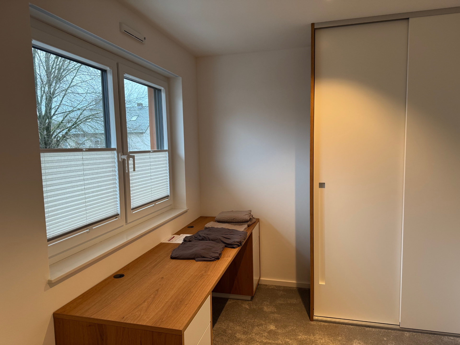 Arbeitszimmer mit langer Schreibtischplatte aus Eiche am Fenster und Einbauschrank.