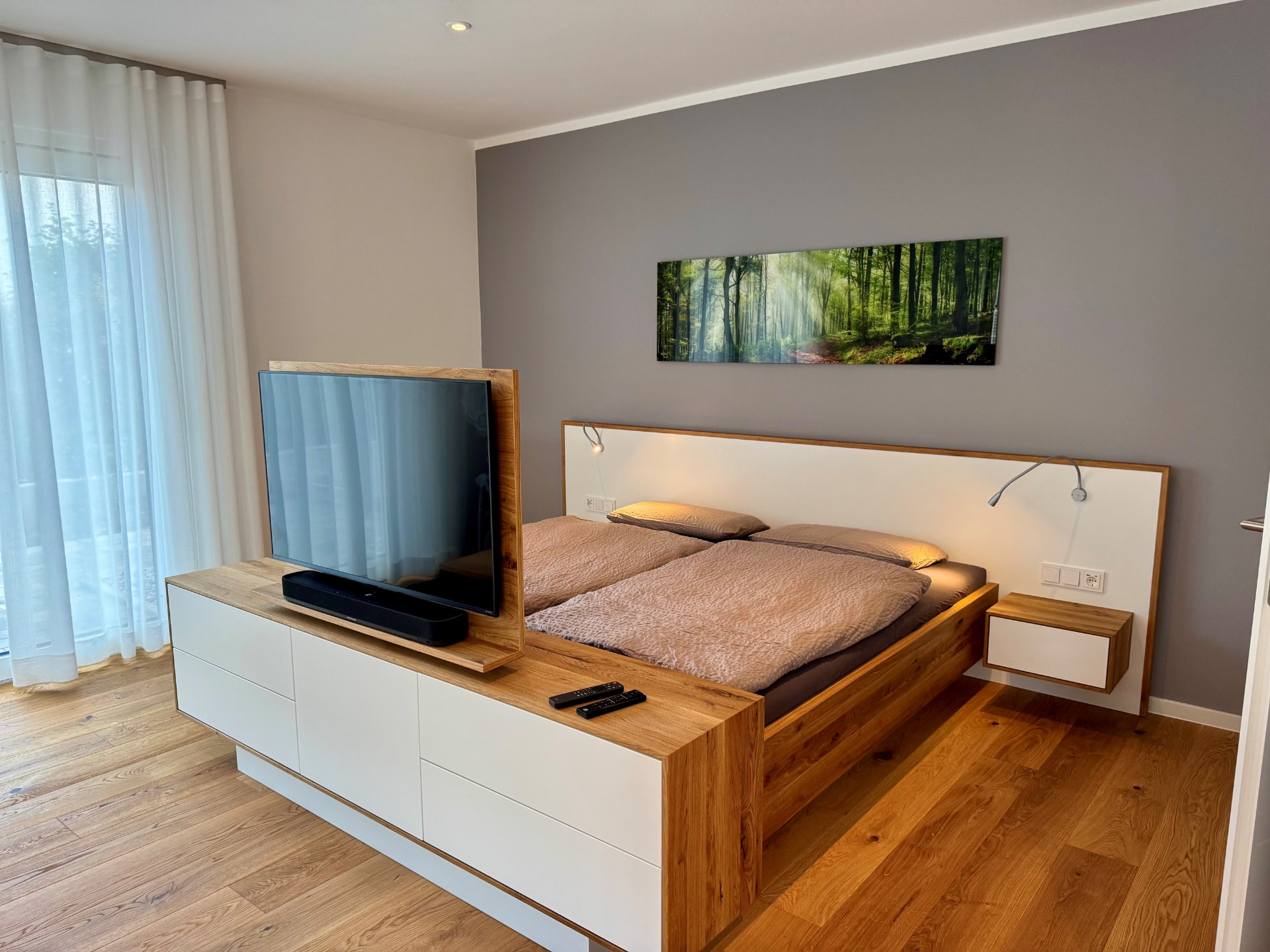 Doppelbett aus Eiche mit beleuchtetem Kopfteil und drehbarem TV am Fußende.