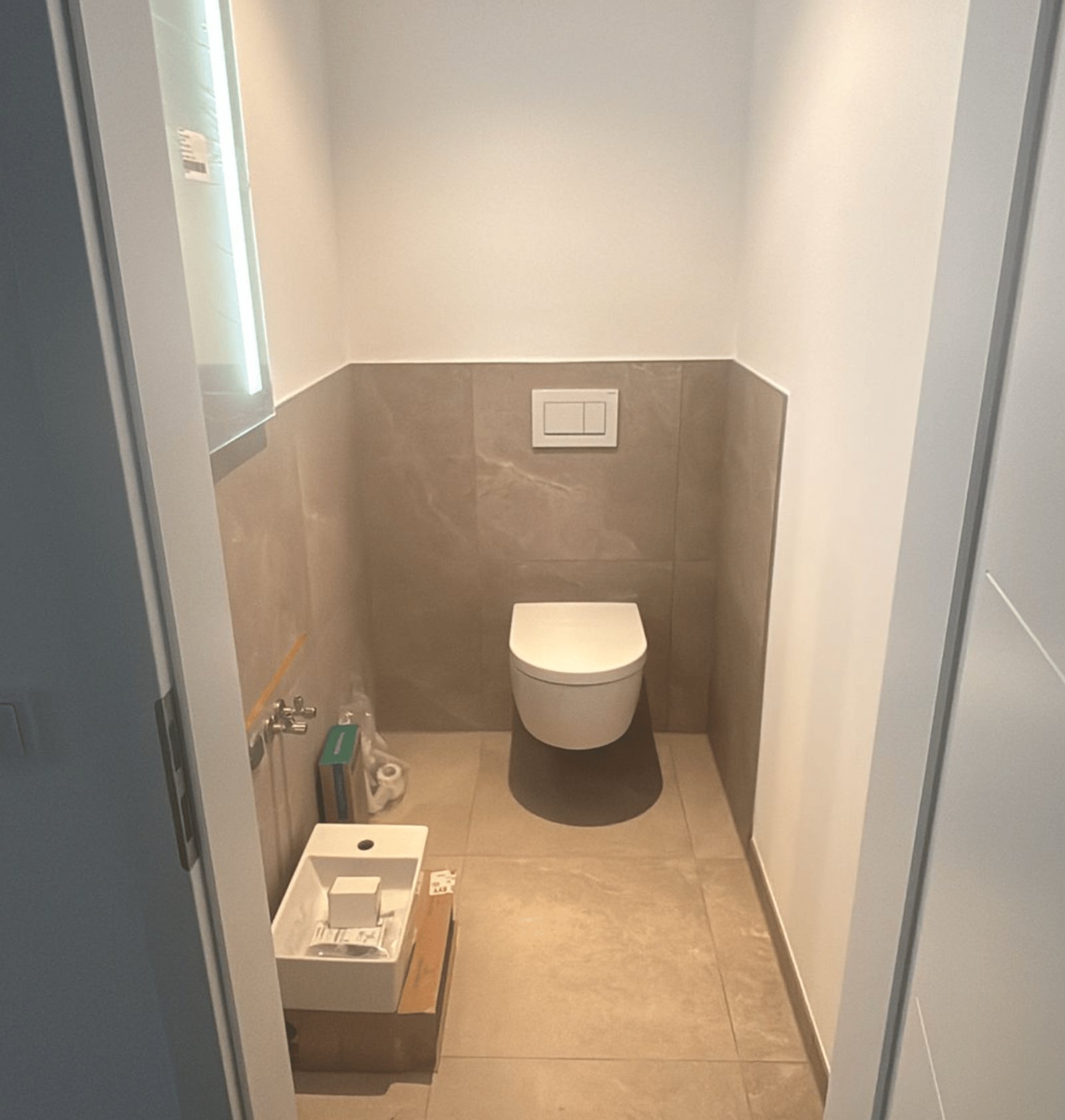 Eine Toilette mit grauen Fliesen und weißer Wand sowie einem kleinen Waschbecken.