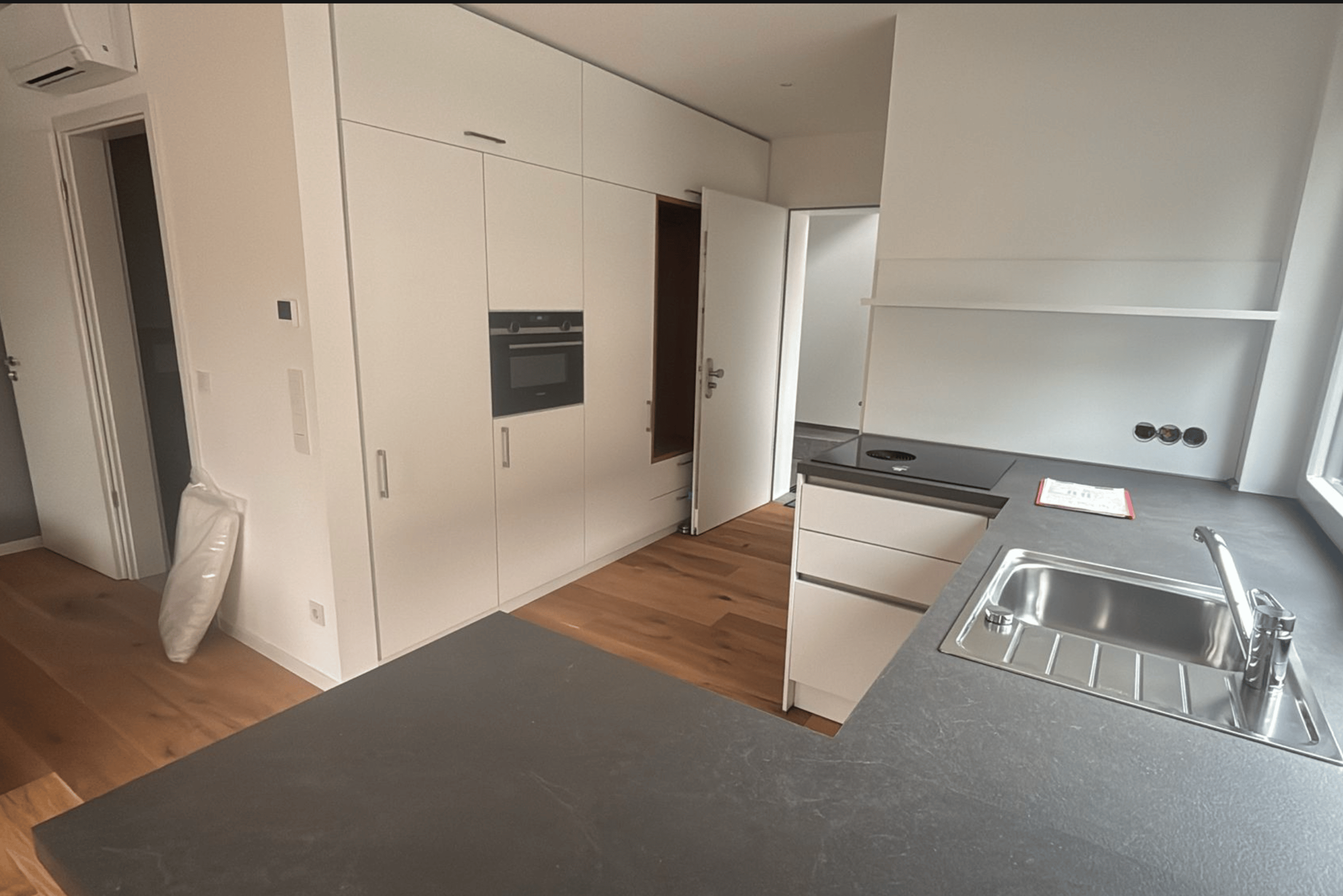 Helle, moderne Küche mit weißen Einbauschränken, integriertem Backofen und Spülbecken.