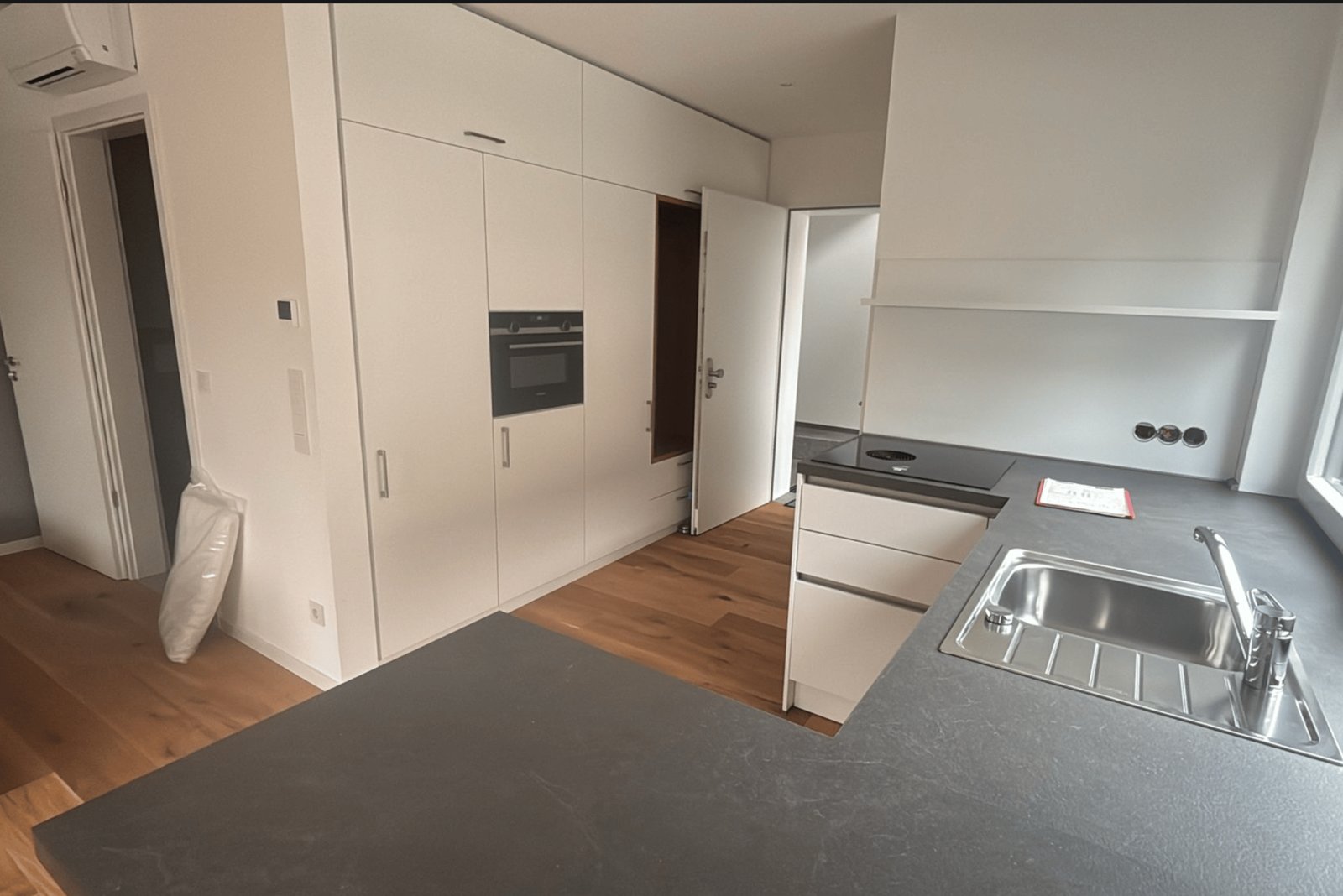 Moderne, weiße Küche mit Holzfußboden, Spüle, Herd und Einbauschränken.
