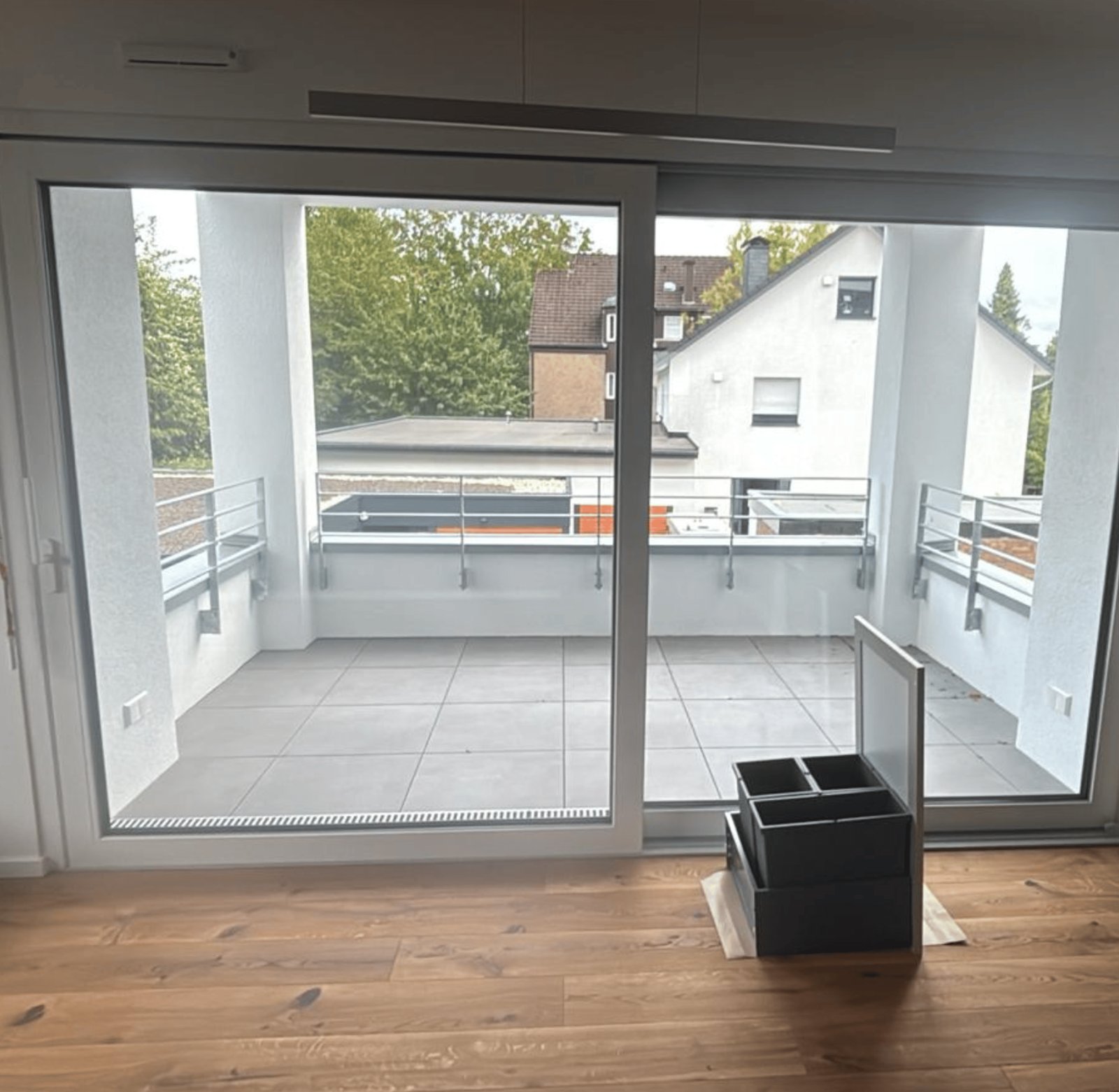 Blick auf einen leeren Balkon mit grauen Fliesen durch eine große Glasschiebetür.