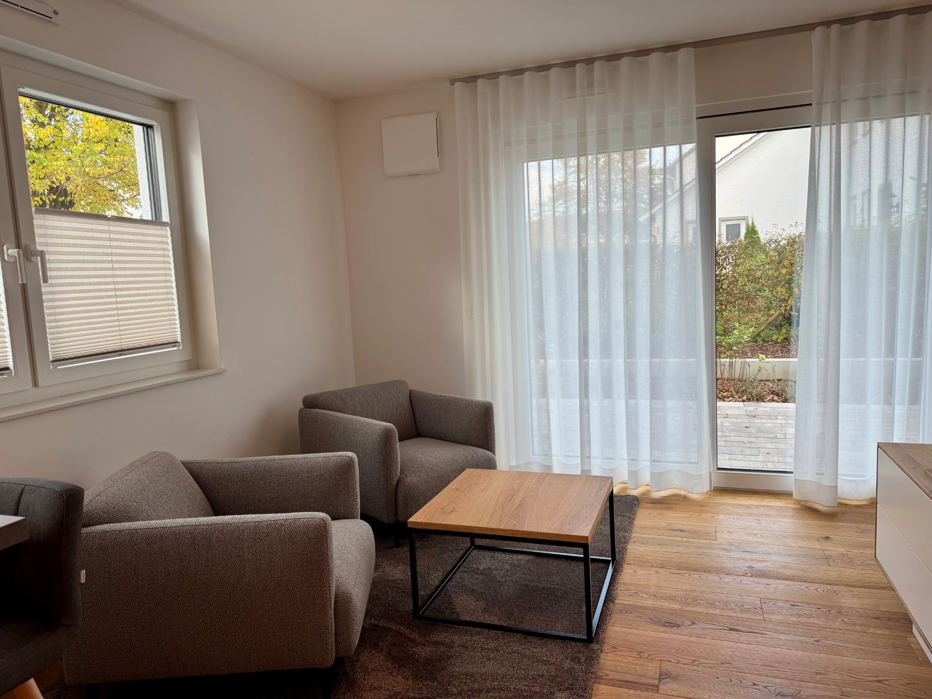 Sitzecke mit zwei Sesseln, Couchtisch und bodentiefer Fenstertür zur Terrasse.